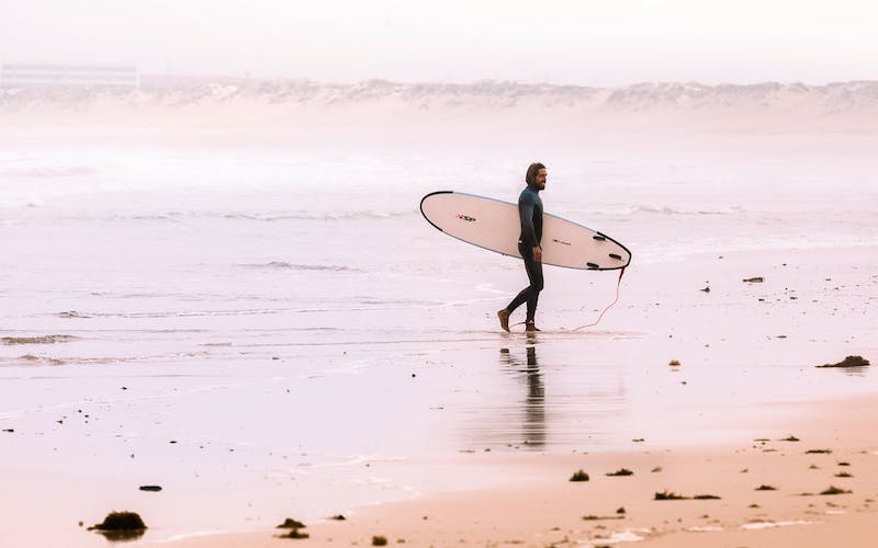 man walking on beach with surfboard