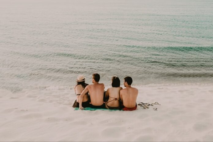 Travelling Group of people sitting on white sandy beach with their backs to the camera