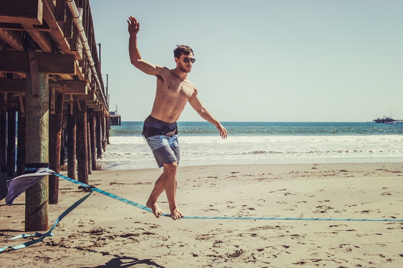 man balancing on slackfline at beach