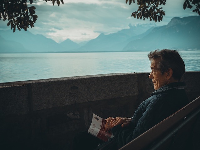 man reading travel book with mountains and river in background