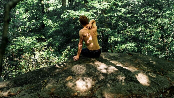 Man sitting on a rock with no shirt on facing away from camera