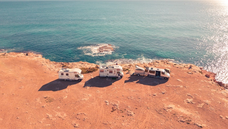 Three RV's parked on orange sand next to a cliff and the ocean